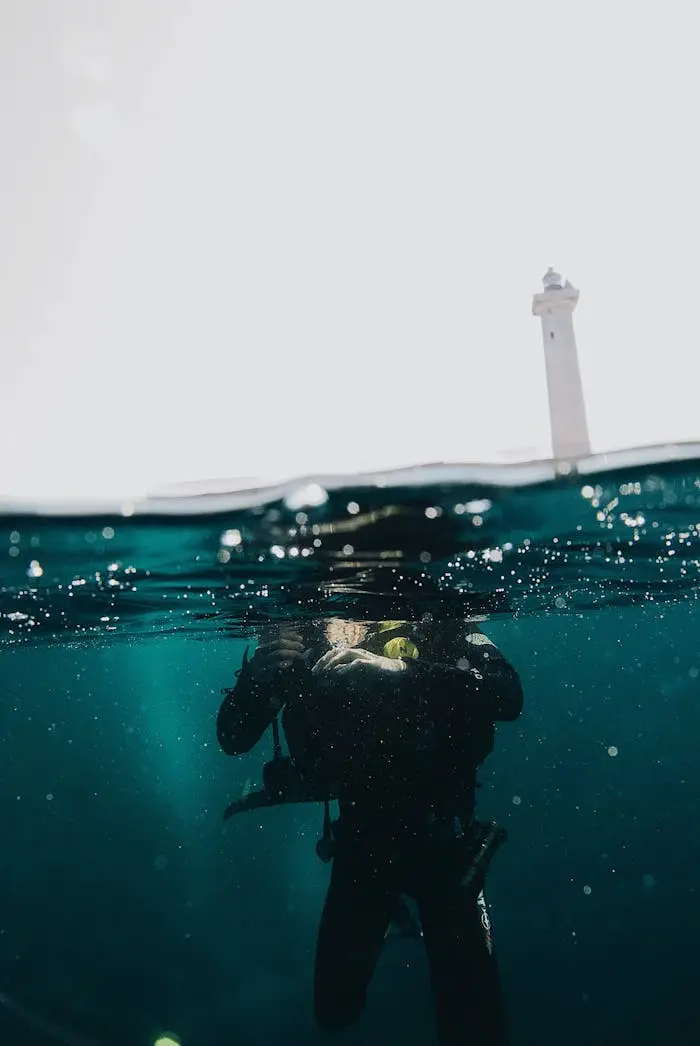 cta-02 Split-level shot of a scuba diver surfacing near a lighthouse.